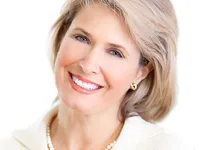 Portrait of a smiling blonde older woman with a pearl necklace and earrings against a white background
