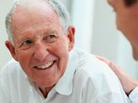 Close-up portrait of a happy elderly man smiling with a hand reassuringly placed on his shoulder