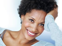 Close-up portrait of a smiling Black woman with short curly dark hair resting her hand against her head