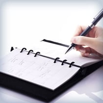 Close-up view of a hand writing with a pen inside a open spiral-bound planner