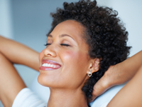 Woman with short curly dark hair resting comfortably with her eyes closed and hands behind her head.